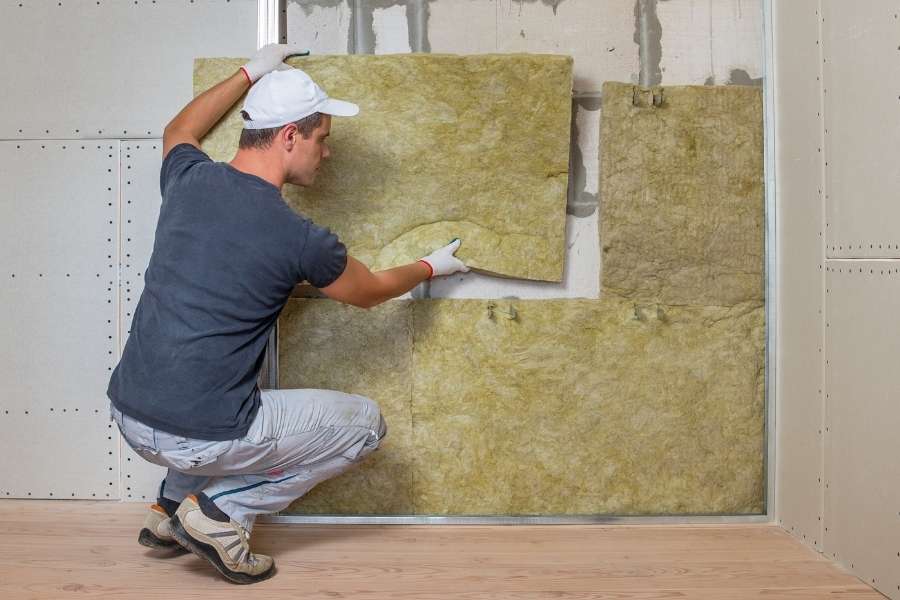 A worker installing mineral wool to improve thermal insulation on an indoor wall.