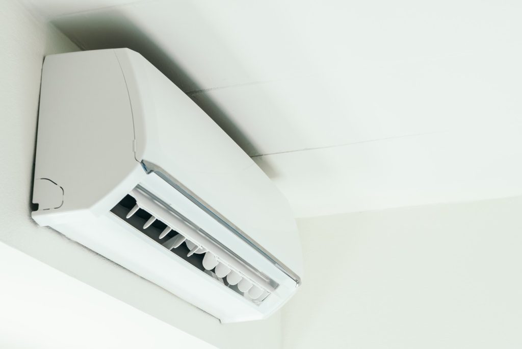Climatiseur mural intérieur blanc, type split, installé au plafond d'une pièce.