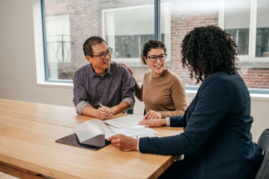 A smiling couple signing papers with a real estate professional to buy a property.
