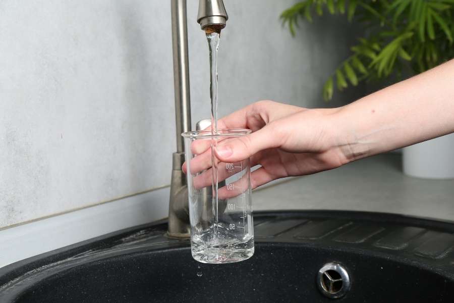 A person holding a measuring glass under a kitchen faucet experiencing low water pressure.